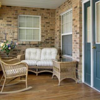 A cozy porch with wicker furniture including a sofa, chairs, and a small table, set against a brick wall.