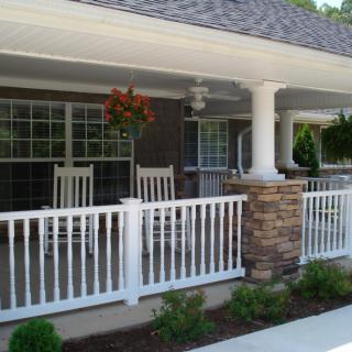 A cozy front porch with rocking chairs and white railing, featuring hanging plants and stone pillars.