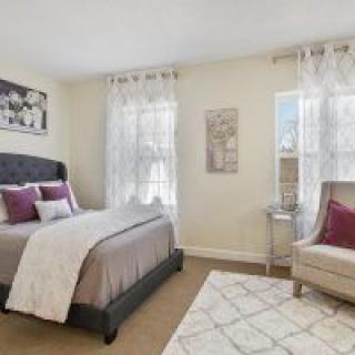 A cozy bedroom with elegant decor, featuring a bed, chair, and natural light from the windows.