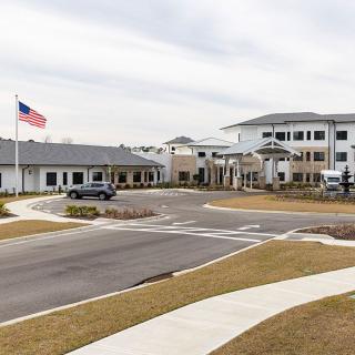 A large institutional building with an American flag and a parking area in front, set against a cloudy sky.