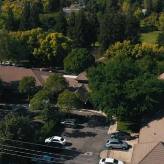Aerial view of a suburban area with buildings, a parking lot, and surrounding trees.