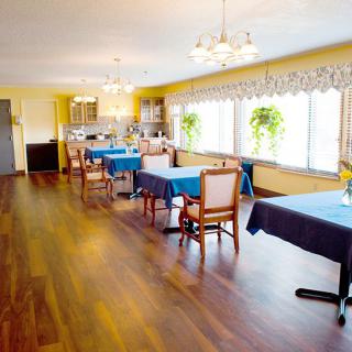 A spacious dining area with wooden floors, blue tablecloth-covered tables, and large windows allowing natural light.