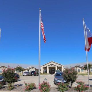 A building entrance with flags and cars parked in the foreground.