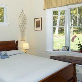 A cozy bedroom with a wooden bed, bedside lamp, and large window overlooking greenery.