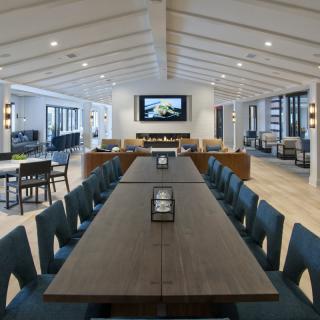 A modern conference room with a long table and chairs, featuring a screen on the wall.