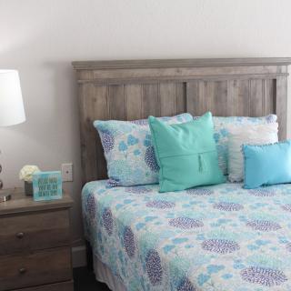 A cozy bedroom with a wooden bedframe, colorful bedding, and decorative pillows alongside a nightstand with a lamp.