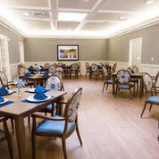 An elegant dining room setup with tables and chairs arranged neatly, featuring blue napkins on each table.