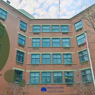 A brick building with multiple windows and trees in the foreground.