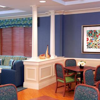 A cozy living and dining area with comfortable chairs, a table, and a sofa, complemented by colorful artwork on the wall.
