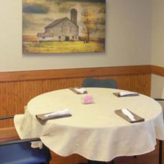 A small dining table set for four in a cozy room with a painting of a barn on the wall.