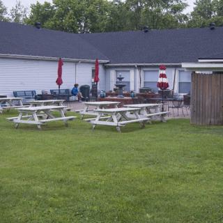 An outdoor patio area with picnic tables and red umbrellas on a grassy lawn.