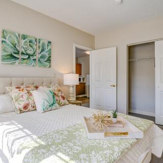 A bright and cozy bedroom with floral decor, featuring a neatly made bed, wall artwork, and an open closet.