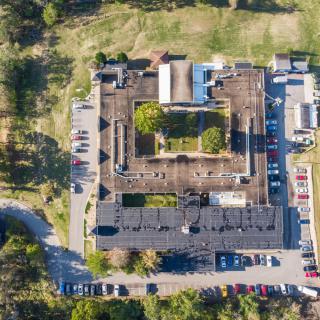 Aerial view of a building with surrounding greenery and a parking lot.