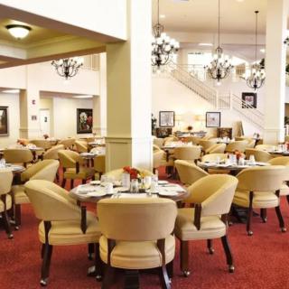 A spacious and elegantly designed restaurant interior with several dining tables and chairs, featuring beautiful chandeliers.