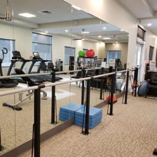 A spacious gym equipped with treadmills, balance bars, and aerobics mats in a well-lit environment.