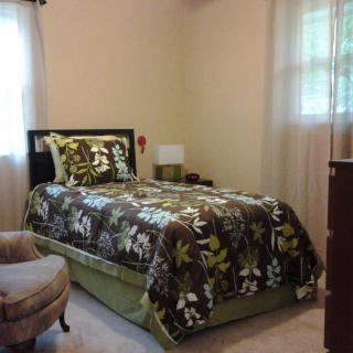A cozy bedroom with a single bed featuring floral bedding, a chair, and a dresser.
