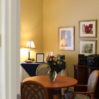 A cozy office space with a round table, chairs, decorative artwork, and a lamp on a side table.