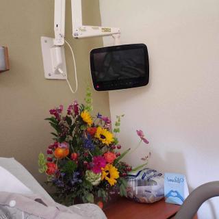 A hospital room with a bouquet of colorful flowers on the bedside table and a small TV mounted on the wall.