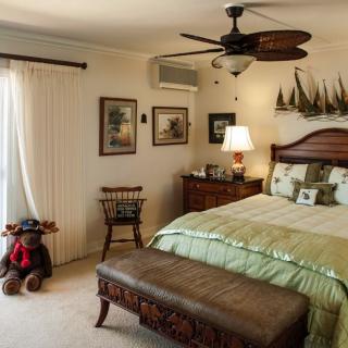 A cozy bedroom with elegant decor, featuring a large bed, ceiling fan, and soft lighting.