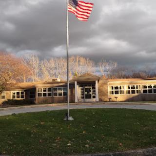 A school building with an American flag waving in front against a cloudy sky.