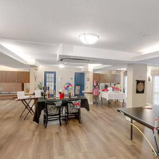 A spacious community room with modern furnishings, including tables, chairs, and wood flooring.