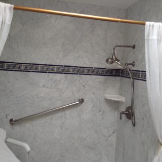 A bathroom shower area with a curtain, grab bar, and tiled wall featuring a decorative border.