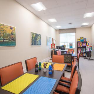 A brightly lit office space featuring tables with colored placemats and comfortable seating, adorned with artwork on the walls.