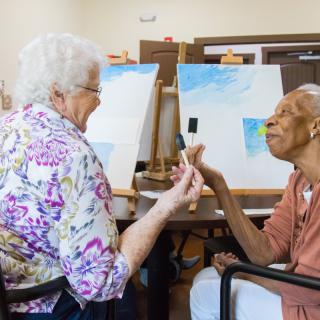 Two elderly individuals enjoying a painting session together in an art class.
