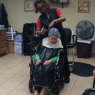 A hairstylist works on an elderly woman's hair in a salon, while she sits comfortably in a wheelchair.