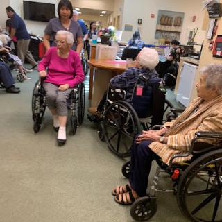 Residents in a care facility engage in a group setting with staff assistance.