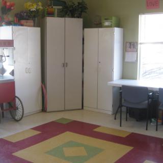 A room with storage cabinets, a desk and chair, and a colorful rug on the floor.