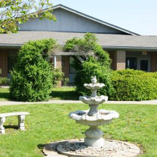 A garden with a fountain and bench in front of a building.