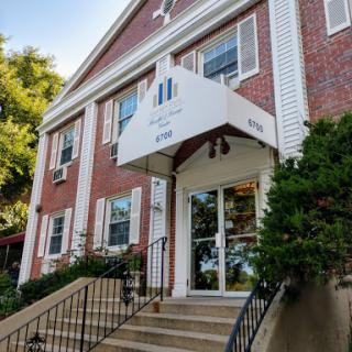 The entrance of a charming brick building featuring a canopy and landscaped surroundings.