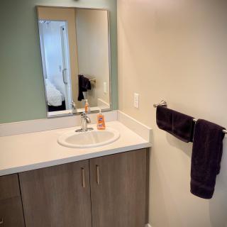 A minimalist bathroom featuring a sink with a mirror above, a set of towels on the wall, and a simple countertop.