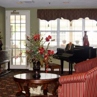 A cozy living room with a grand piano, floral arrangement on a table, and striped armchairs.