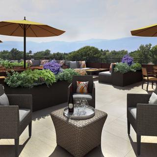 A stylish outdoor patio with comfortable seating and umbrellas, surrounded by greenery.
