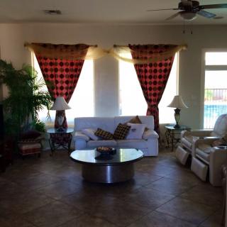 A cozy living room with a sofa, armchairs, and a central glass coffee table, complemented by red checkered curtains and indoor plants.