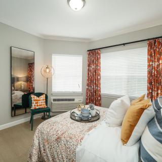 A modern and cozy bedroom with a decorative mirror, colorful pillows, and patterned curtains creating a warm and inviting atmosphere.