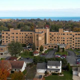 An aerial view of a multi-story building near the ocean, surrounded by residential homes and autumn foliage.