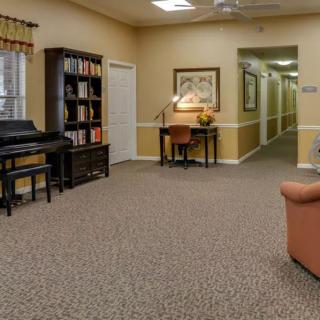 A cozy living area with a piano, bookshelf, desk, and sofa leading to a hallway.