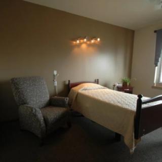 A minimalist bedroom with a bed, armchair, and wall-mounted lamp.