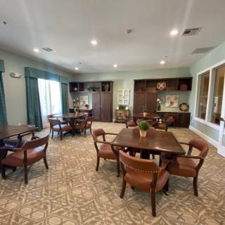 A cozy dining room with several tables and chairs, decorated with warm lighting and carpeted floors.