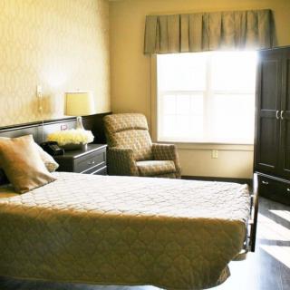 A cozy bedroom with a single bed, armchair, and a sunlit window.