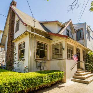 A charming traditional-style house with a well-maintained front yard and large windows, bathed in sunlight.