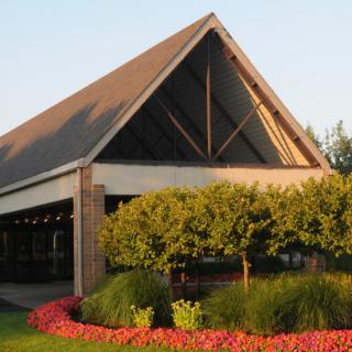 A modern building with a triangular roof surrounded by landscaped gardens and vibrant flowers.