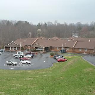 A view of a building with a parking lot surrounded by grassy areas and trees on an overcast day.