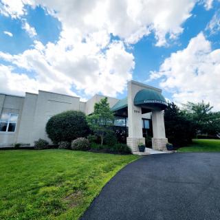 A building with an arched entrance and a driveway, set against a backdrop of a partly cloudy sky.