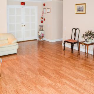 A spacious living room with wooden flooring, featuring a sofa and two chairs, along with decorative elements like a framed picture and a vase.