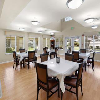 A spacious dining room with multiple tables and chairs, featuring large windows and modern lighting.