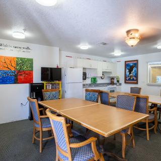 A cozy kitchen and dining area featuring wooden tables and chairs, adorned with colorful artwork on the walls.
